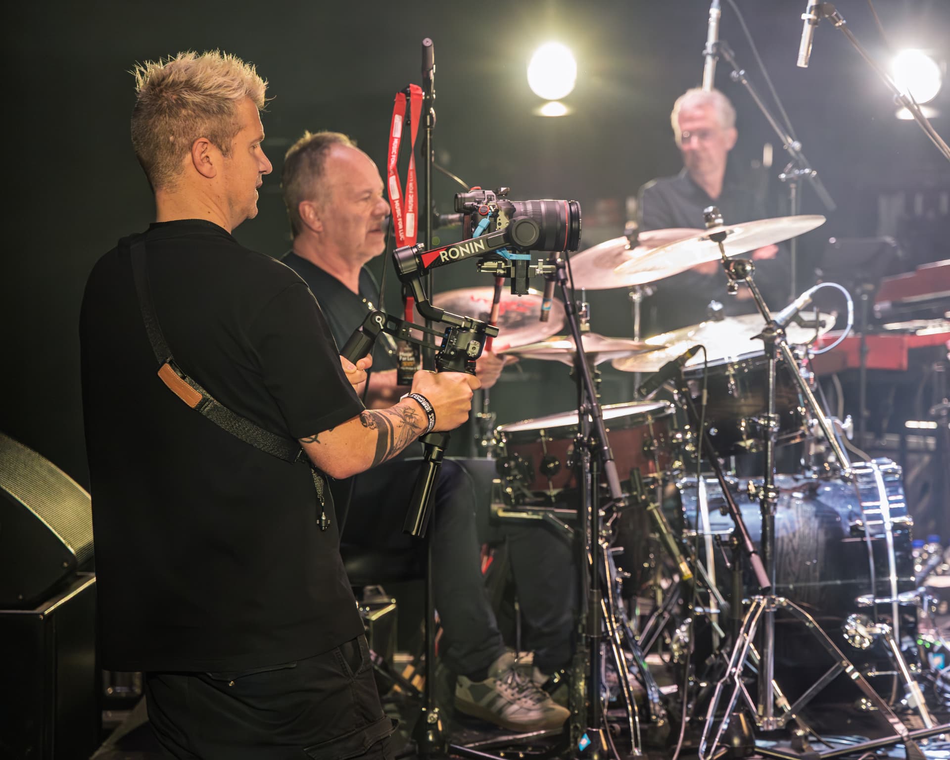 Sam filming with a Ronin gimbal beside the drummer on stage